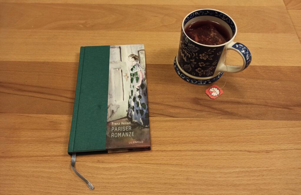 Franz Hessels Buch "Pariser Romanze" liegt auf einem Holztisch. Rechts daneben eine blau-weiße Tasse Tee.